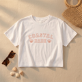 White t-shirt with 'Coastal Babe' text on a sandy background with sunglasses, shells, and a woven bag.