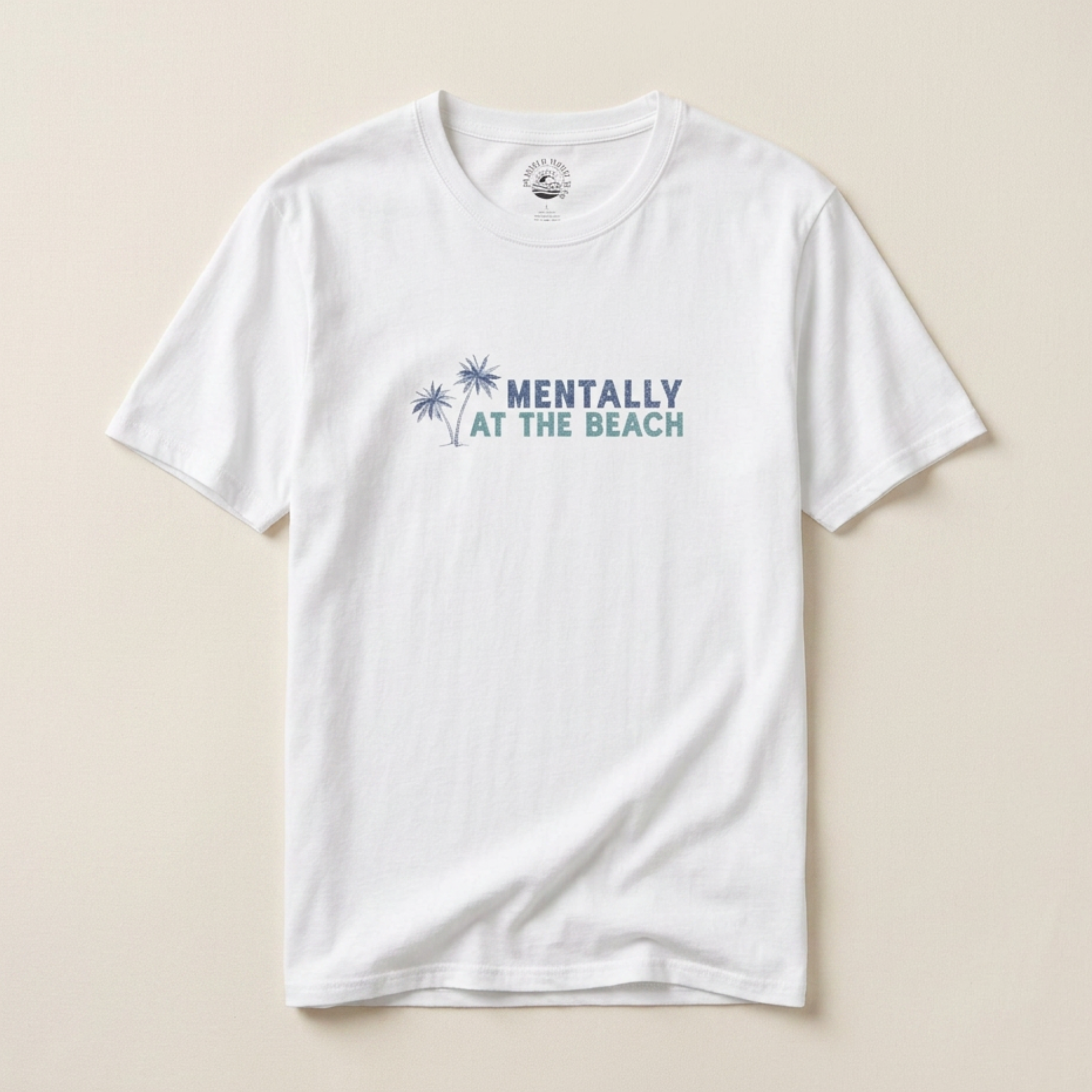 White t-shirt with 'Mentally at the Beach' text and palm tree graphics on a beige background