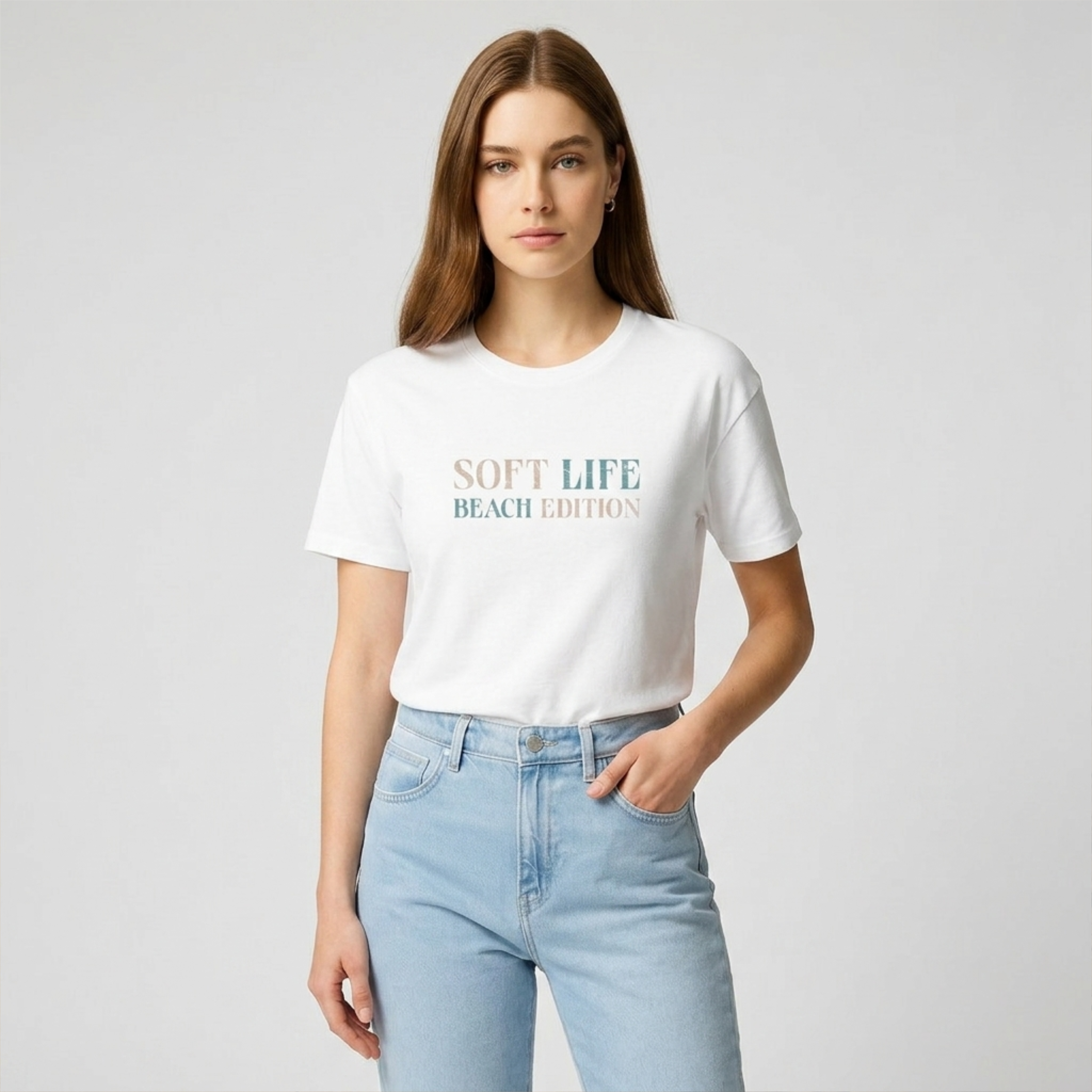 Woman wearing a white t-shirt with 'Soft Life Beach Edition' text and light blue jeans on a plain background
