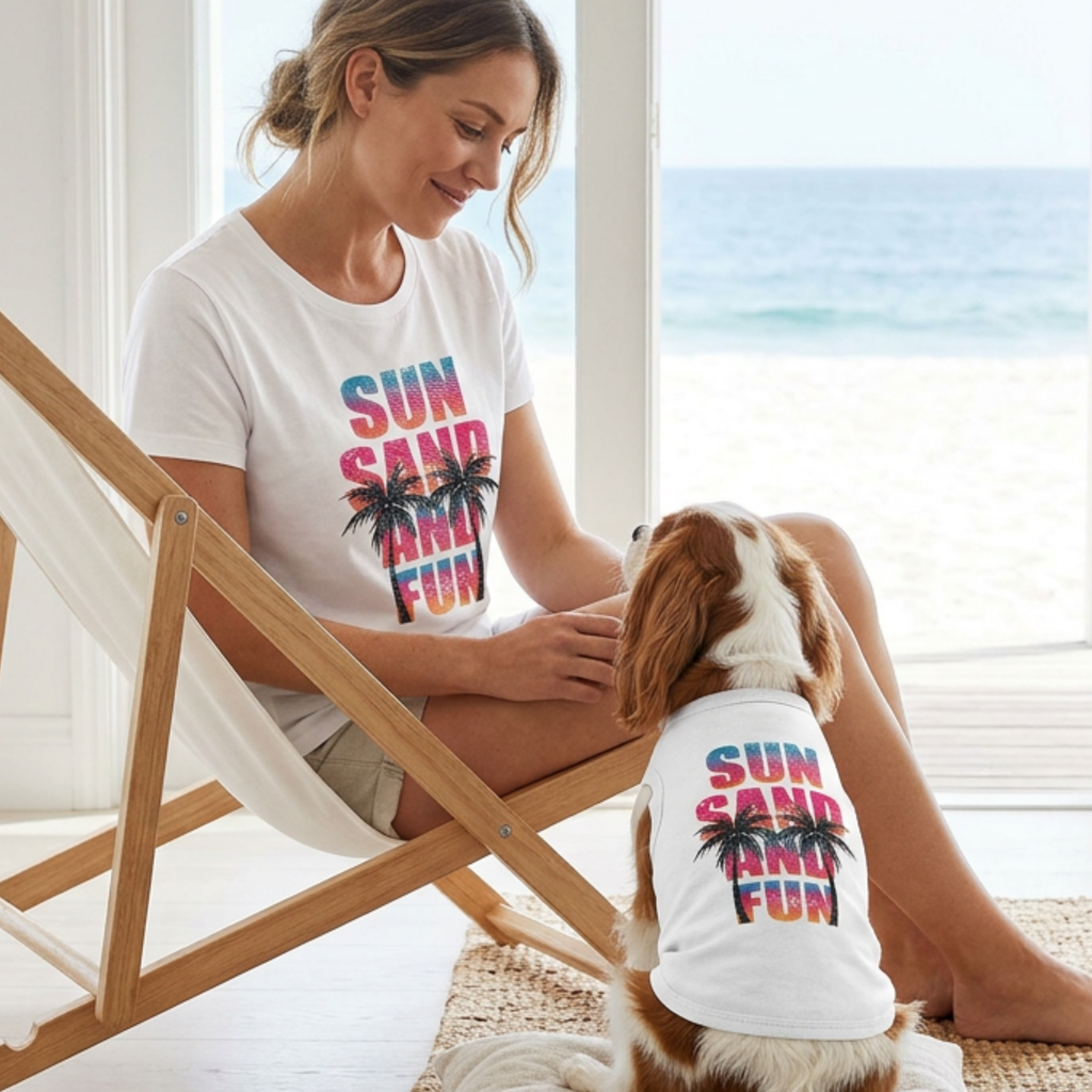 Woman and dog wearing white matching 'Sun, Sand, and Fun' shirts by a window with a view of the ocean.